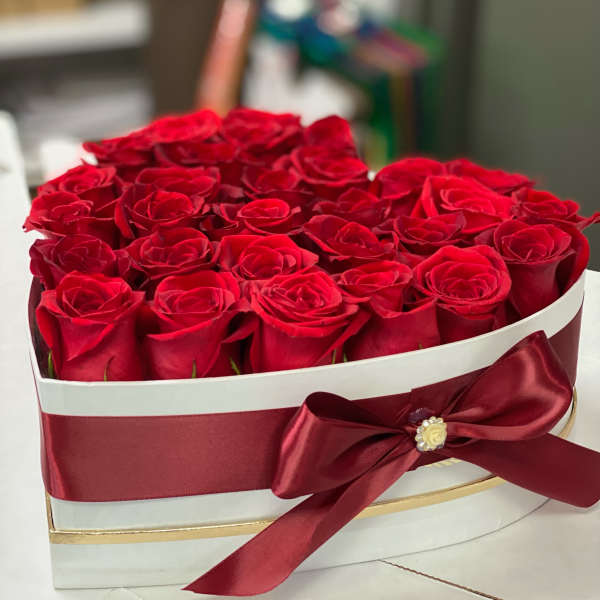 Heart-shaped box filled with red roses and a burgundy ribbon