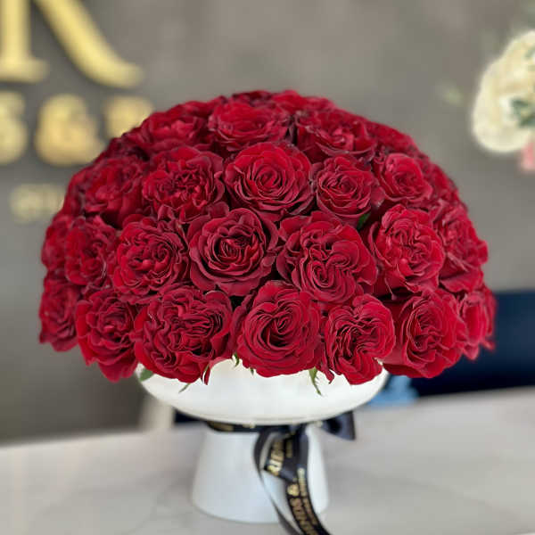 Round bouquet of red roses in a white vase with a black ribbon