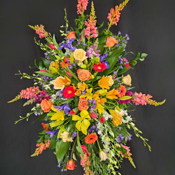 Tall standing spray of yellow lilies, orange roses, and bright mixed flowers on a black background
