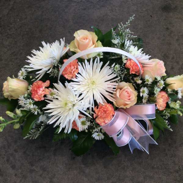 Basket arrangement of white spider mums, peach roses, and pink carnations with a ribbon handle