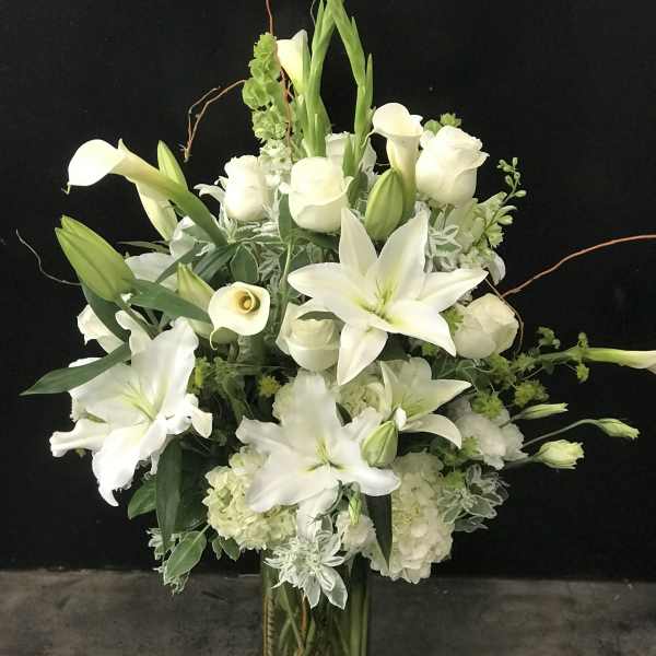 White lilies, calla lilies, and roses arranged in a tall glass vase