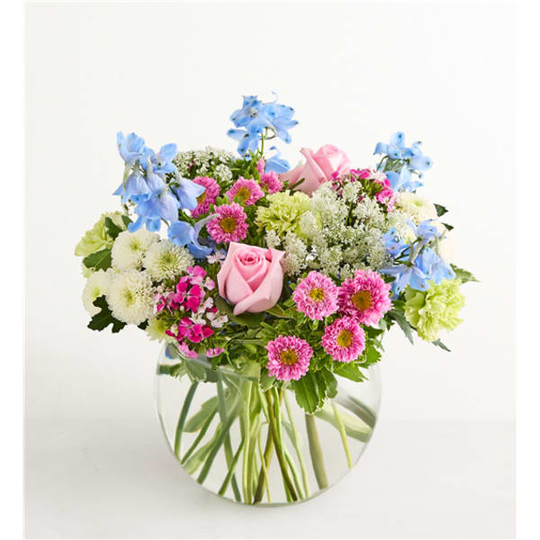 Mixed bouquet of pink roses, blue flowers, and daisies in a clear glass vase