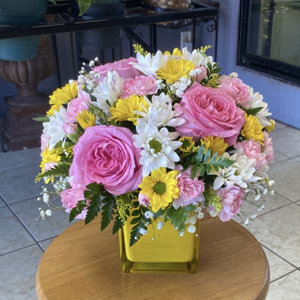 Pink roses, yellow and white daisies, and carnations in a yellow vase