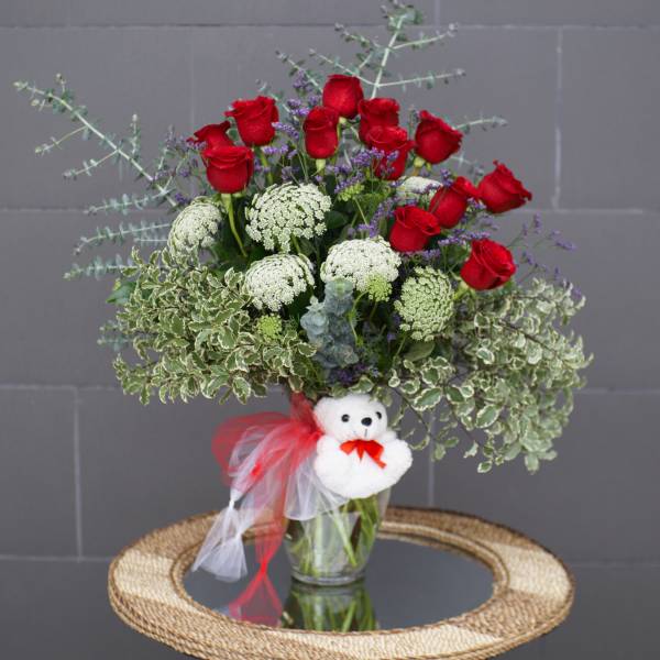 Bouquet of red roses with white filler flowers in a glass vase, decorated with a teddy bear