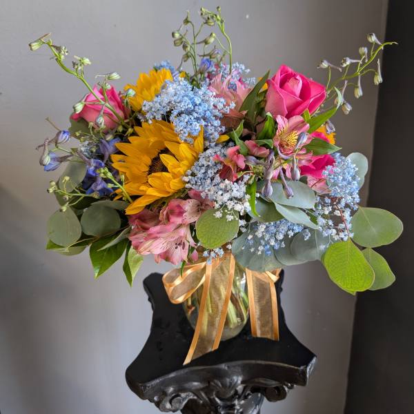 Bouquet of sunflowers, pink roses, and blue filler flowers in a glass vase