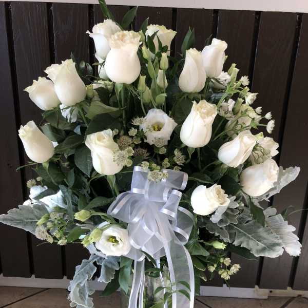 White roses and lisianthus in a glass vase with a white ribbon