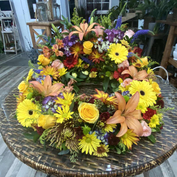 Large colorful floral wreath with lilies, roses, and daisies on a round table