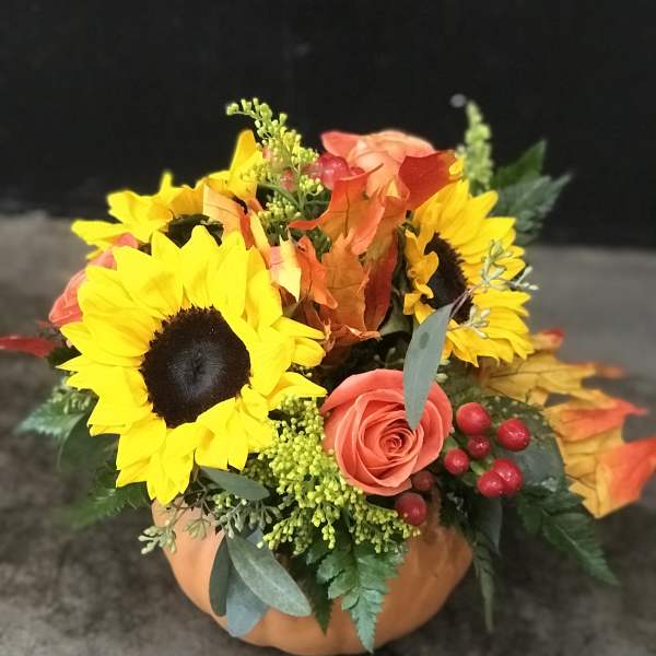 Pumpkin-shaped container with sunflowers, a coral rose, and autumn leaves