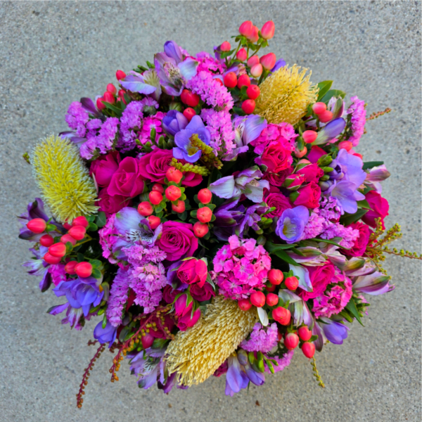 Round bouquet of pink, purple, and yellow flowers on a gray surface
