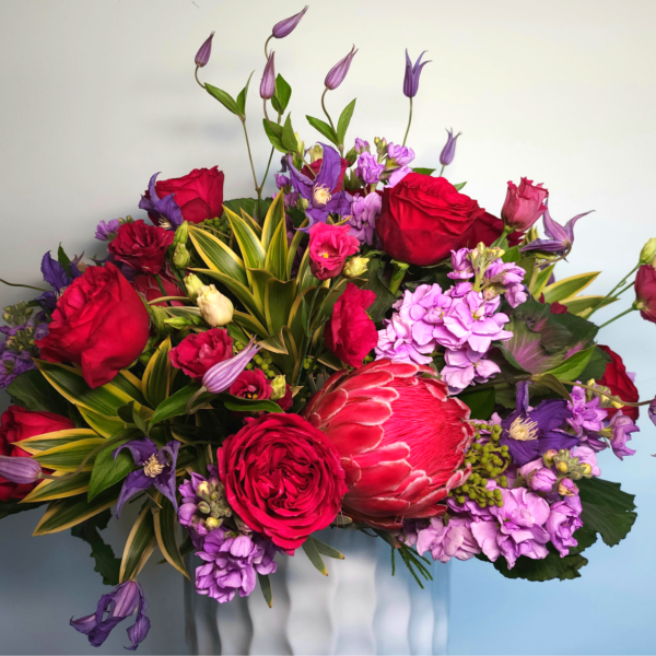 Bouquet of red roses, purple blooms, and a pink protea in a vase