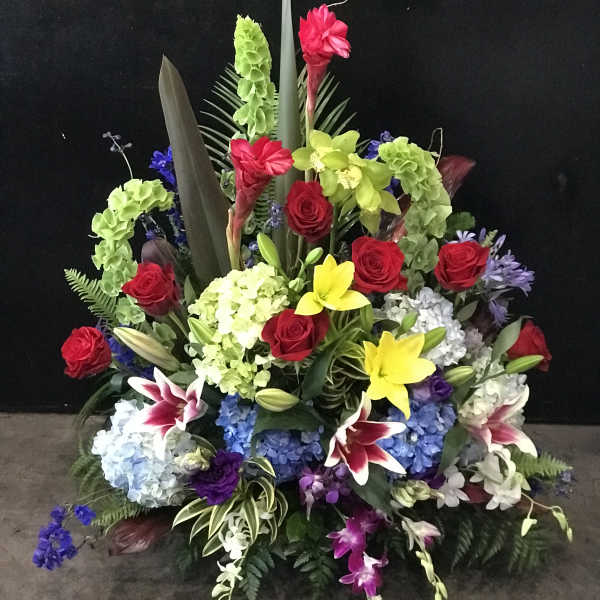 Large standing floral arrangement with red roses, lilies, and hydrangeas