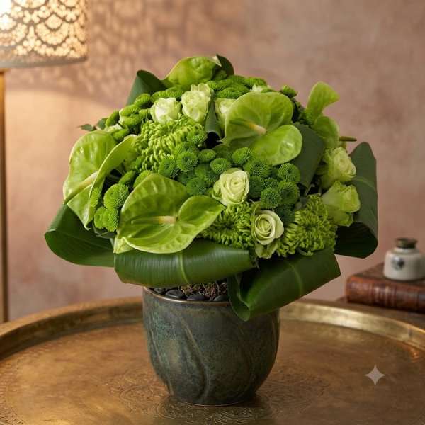 Green floral arrangement in a dark vase with broad leaves and pale blooms