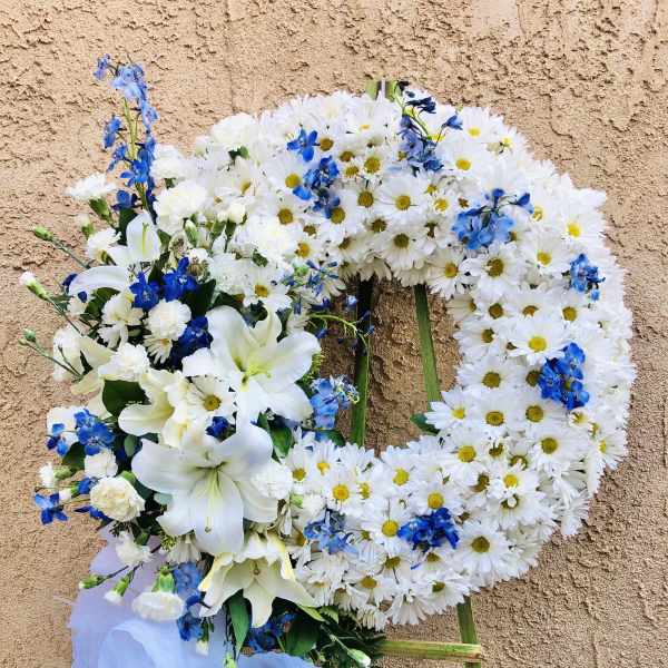 White daisy wreath with blue flowers and lilies on a stand