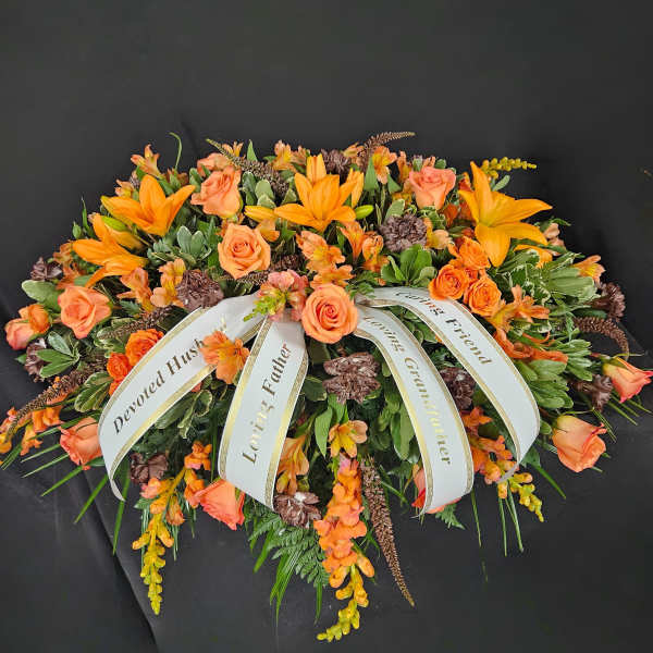 Orange lilies and roses casket spray with white sympathy ribbons on a dark background