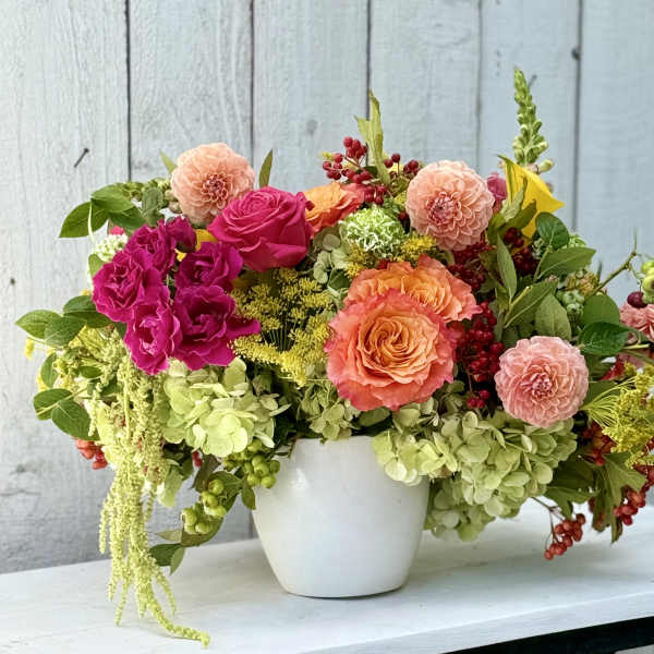 Mixed bouquet of pink, peach, and green flowers in a white pot