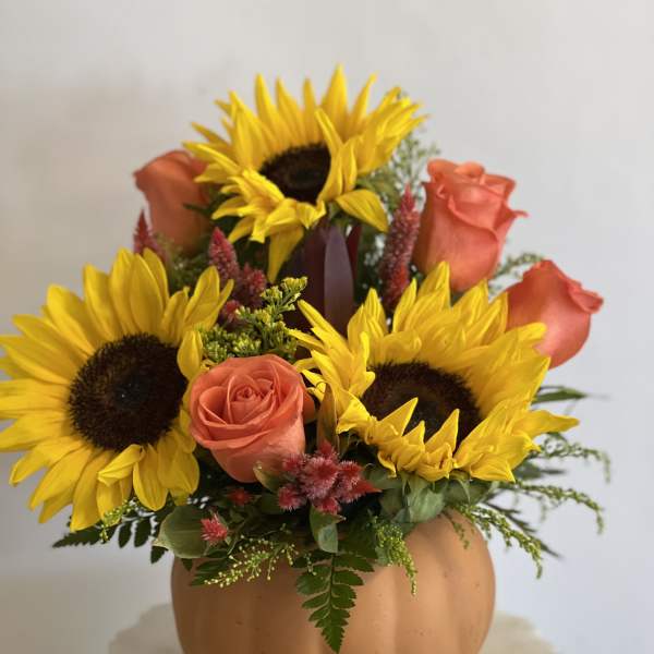 Sunflowers and coral roses arranged in a pumpkin-shaped vase