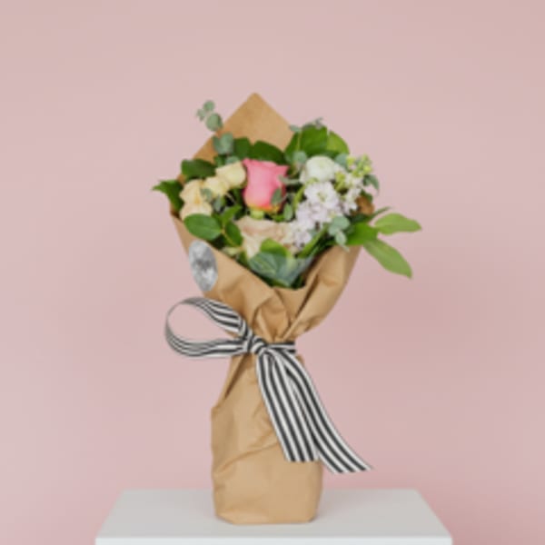 Wrapped bouquet of pink and cream roses with a striped ribbon