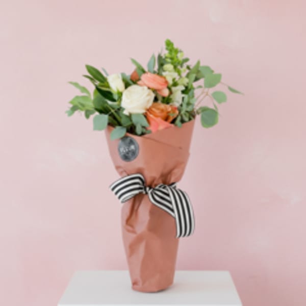 Wrapped bouquet of peach and white roses with greenery and a striped ribbon