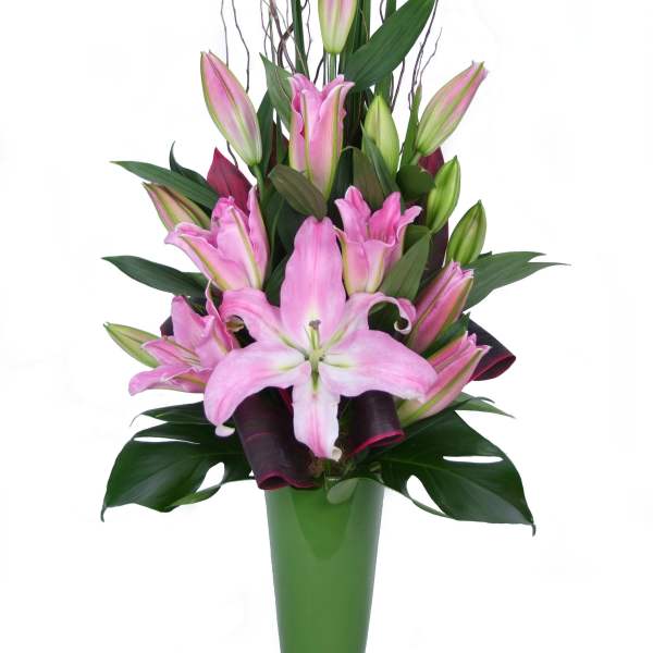 Pink lilies arranged in a tall green vase with dark foliage