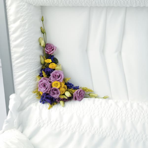 Purple and yellow floral spray arranged on a white casket