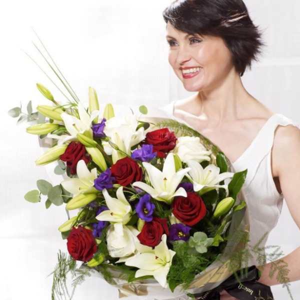 Woman holding a bouquet of red roses, white lilies, and purple flowers