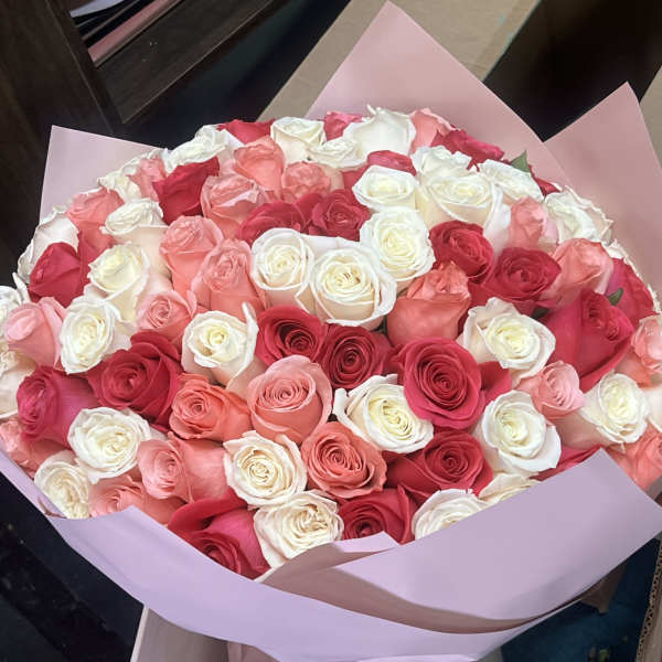 Large bouquet of pink, red, and white roses wrapped in pale pink paper