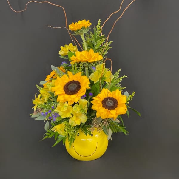 Sunflower arrangement in a yellow smiley-face vase with curly branches