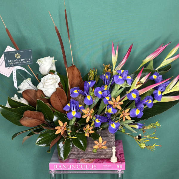 Arrangement of white roses, purple irises, and pink tropical blooms in a rectangular vase