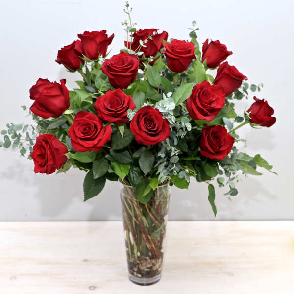 Tall clear vase of long-stemmed red roses with accent foliage