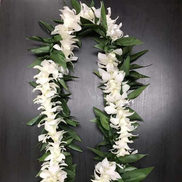 White orchid lei with green leaves on a dark surface