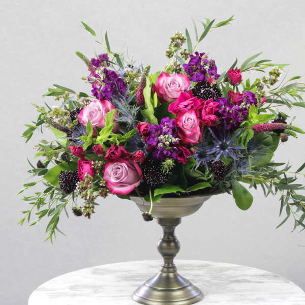 Pink and purple rose arrangement in a silver pedestal vase