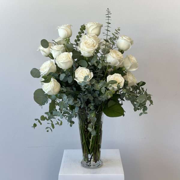 White roses arranged in a tall glass vase with eucalyptus foliage