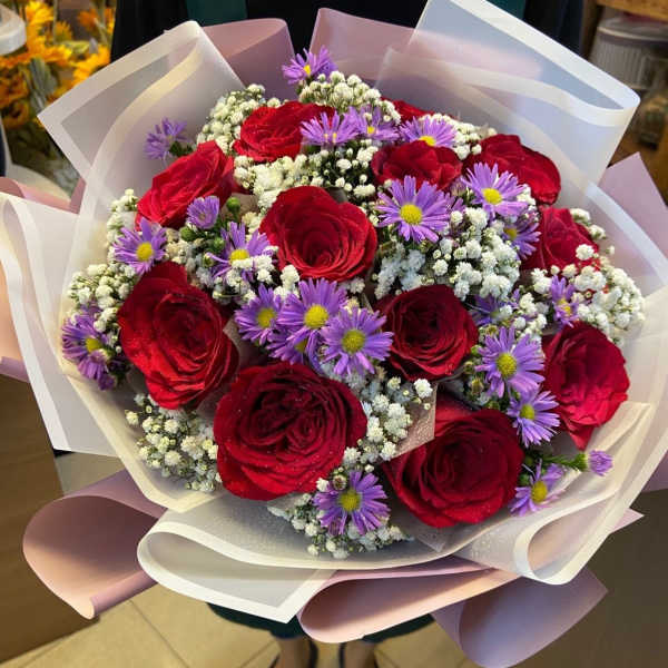Bouquet of red roses and purple daisies wrapped in white paper