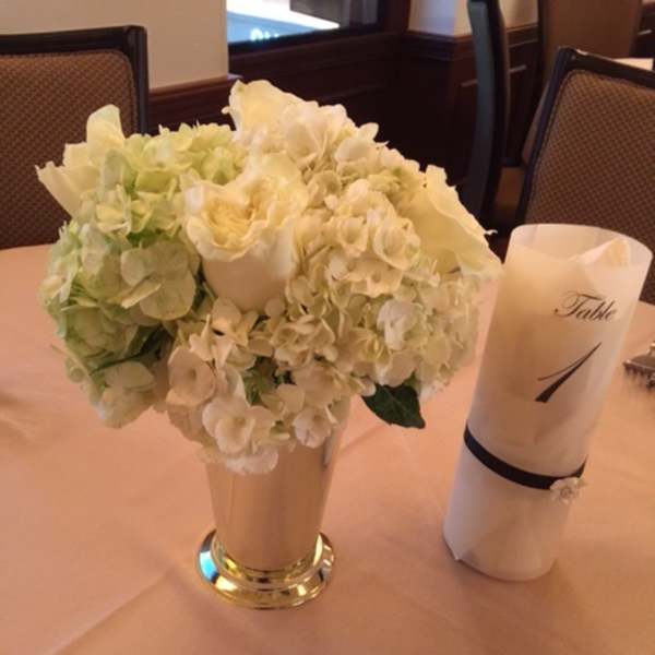 White floral centerpiece in a tall vase beside a rolled napkin