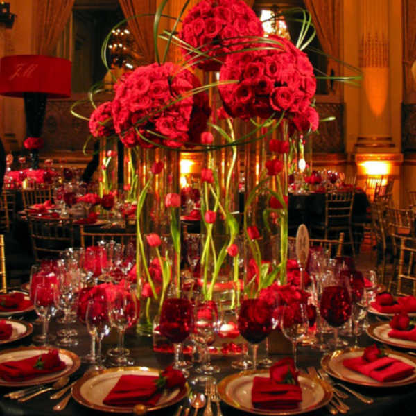 Tall red rose centerpieces in glass vases on a formal banquet table