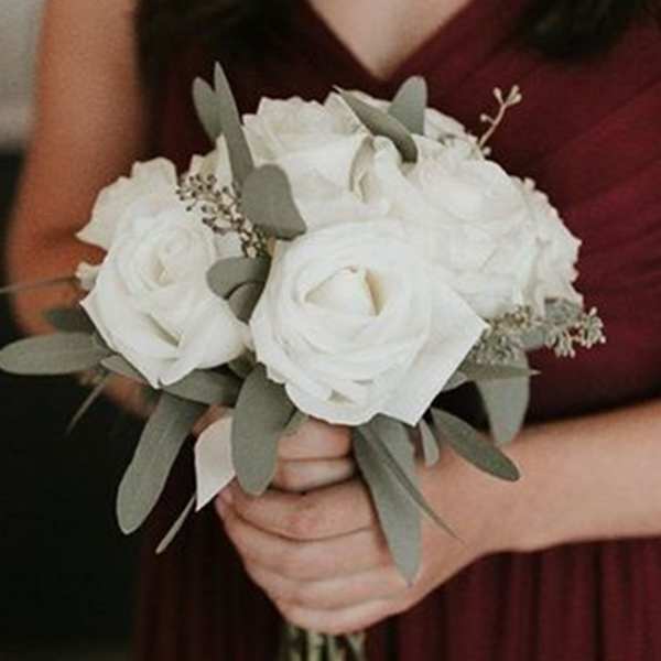 White rose bouquet with eucalyptus held by a person in a burgundy dress