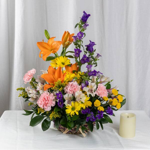 Mixed bouquet with orange lilies, purple bells, pink carnations, and yellow daisies in a basket