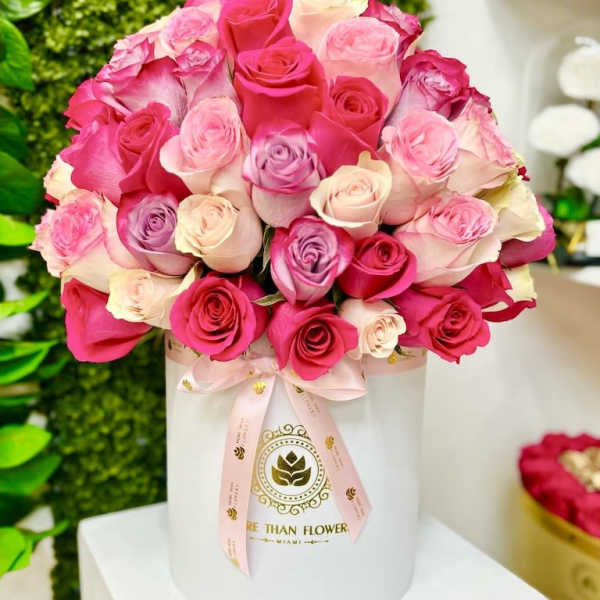 Round hat box arrangement of pink, cream, and lavender roses in a white cylinder box with ribbon.