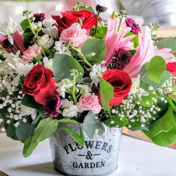 Mixed pink and red flower arrangement in a metal bucket