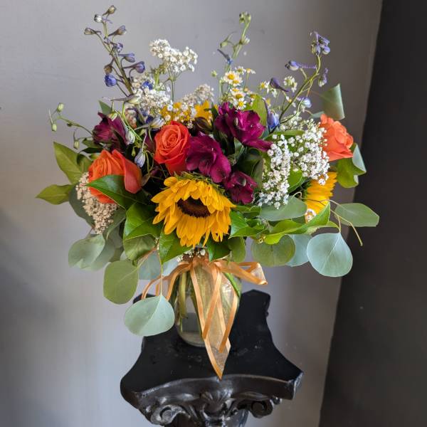 Mixed bouquet with sunflowers, roses, and purple blooms in a glass vase