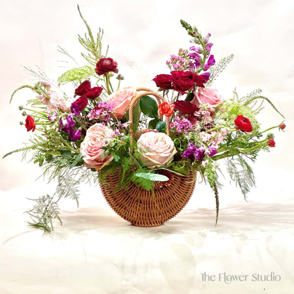 Basket arrangement of pink and red roses with purple flowers