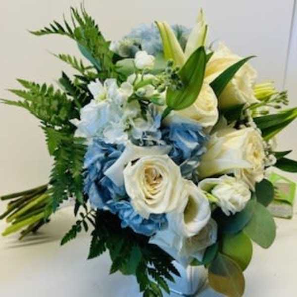 Bouquet of white roses, blue flowers, and lilies with greenery