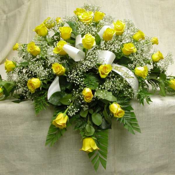 Yellow roses arranged with baby's breath and white ribbon on a draped cloth