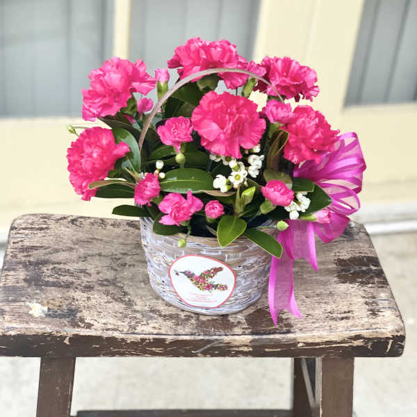 Pink carnations in a woven basket with a ribbon bow
