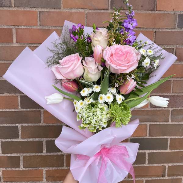 Bouquet of pink roses, tulips, and purple flowers wrapped in lavender paper
