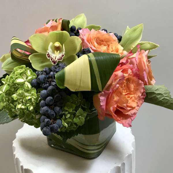 Bouquet of orange roses, green orchids, and hydrangeas in a square vase