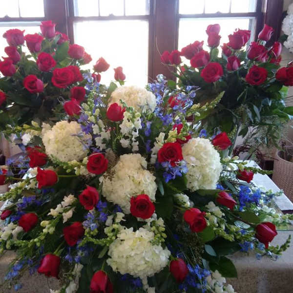 Large floral arrangement of red roses, white hydrangeas, and blue flowers