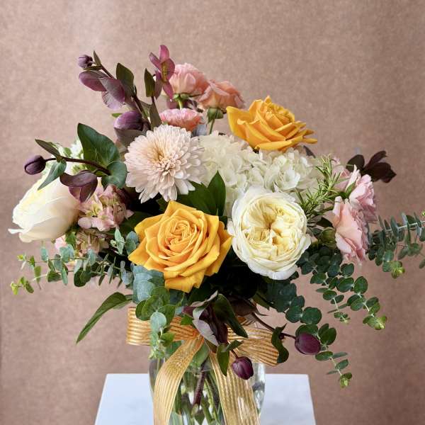 Bouquet of yellow, white, pink, and purple flowers in a glass vase with a ribbon