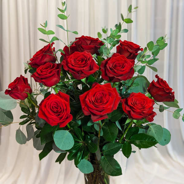 Red roses arranged in a clear glass vase with eucalyptus