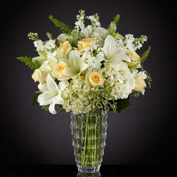 White and pale yellow floral arrangement in a clear glass vase